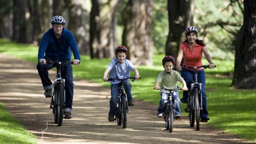 Family on bikes enjoying the gardens riding on a path between trees at Clumber Park, Nottinghamshire